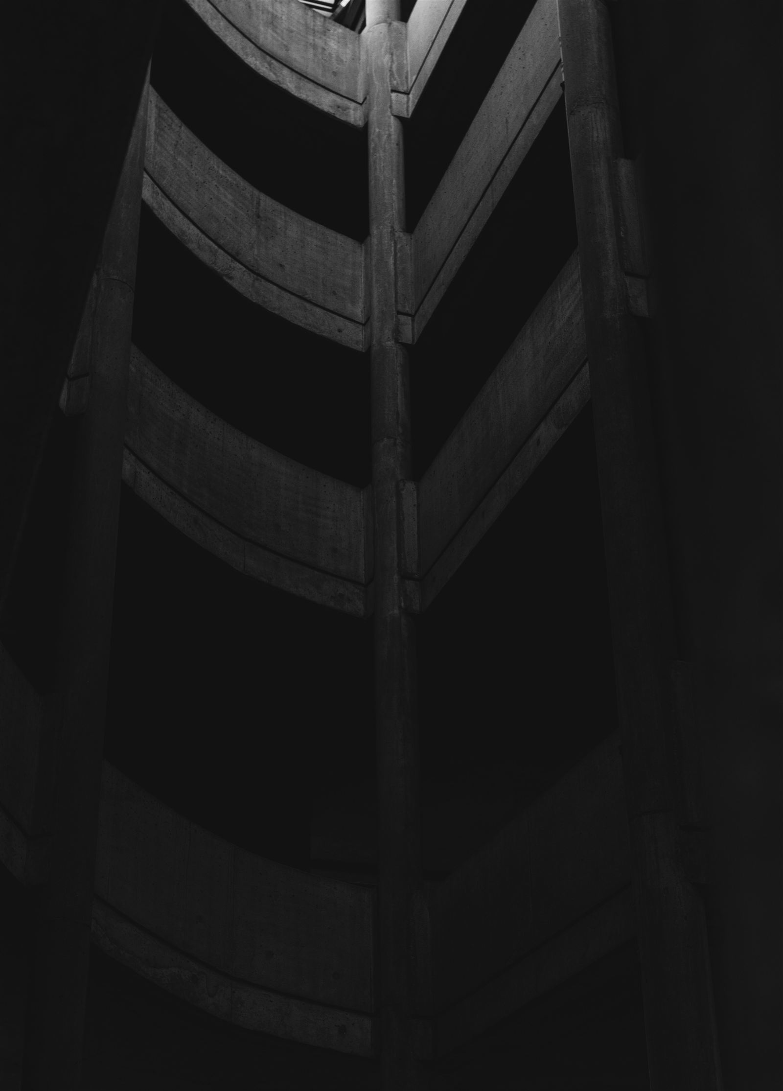 A brutalist concrete stairwell shot from below, evoking turbine tower scaffolding.